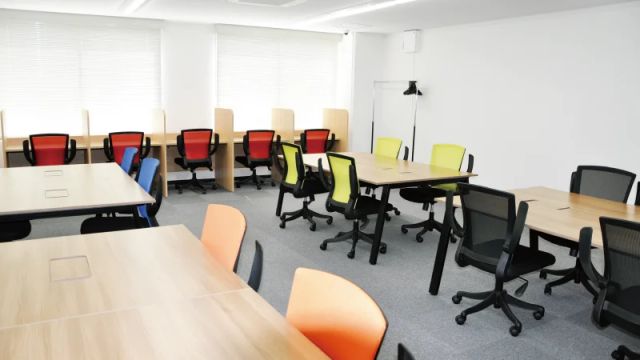 白を基調とした自習室Best Focusのオープンスペース。木目の長机に赤・青・緑・橙のチェアが並ぶ明るい室内